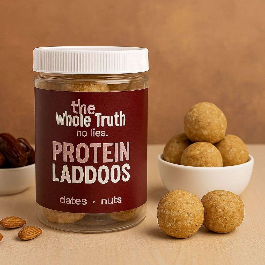 Pack of The Whole Truth’s Protein Laddoos with a few round laddoos placed on a plate, showcasing their rich, nutty texture.