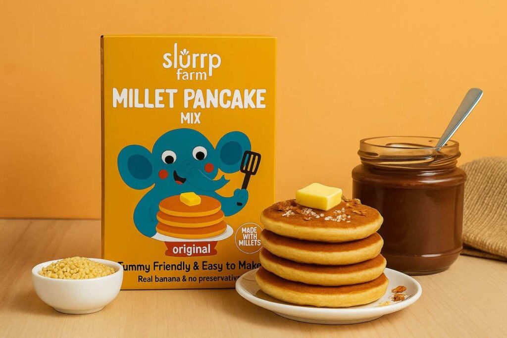 Box of Slurrp Farm’s Millet Pancake Mix placed beside a stack of fluffy pancakes topped with fruits and honey.